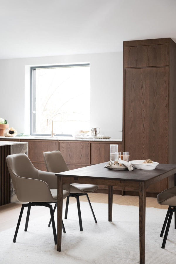 Matbord i mörkt trä med moderna stolar i beige och grå, placerats i ljust kök med matchande skåp