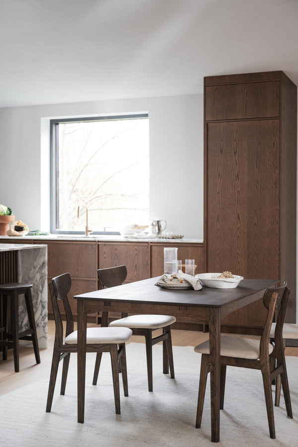 Matgrupp i mörkt trä med fyra stolar och vita dynor i modern Skandinavisk matsal med köksinredning