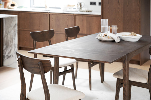 Matbord i mörkt trä med stolar i vardagsrum med vita kuddar och glasvatten på bordet