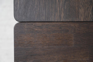 Närbild på mörkt träfanér med synlig struktur och rundade hörn på möbelpaneler