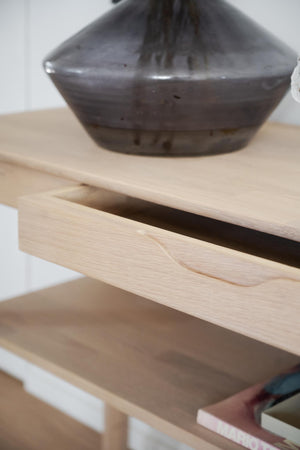 Ljust träbyrå med utdragen låda och dekorativ mörkgrå vas på toppen