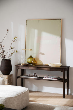 Konsolbord i mörkt trä med spegel, vas och dekorativa glasföremål i modern skandinavisk inredning