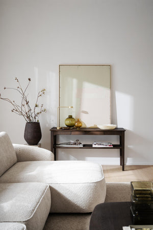 Minimalistiskt vardagsrum med beige soffa, mörkt sidobord, stor spegel och dekorativa vaser i naturliga toner