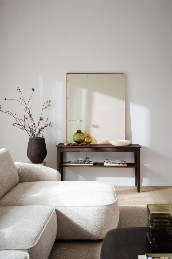 Minimalistiskt vardagsrum med beige soffa, mörkt sidobord, stor spegel och dekorativa vaser i naturliga toner