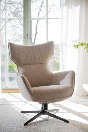 Beige vilstol med hög rygg och svart fotställ vid fönster i ljust vardagsrum