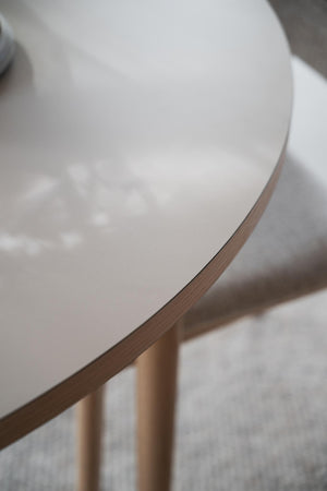 Rund vit bordsskiva med träkant och träben i ljust trä, närbild av modern skandinavisk design