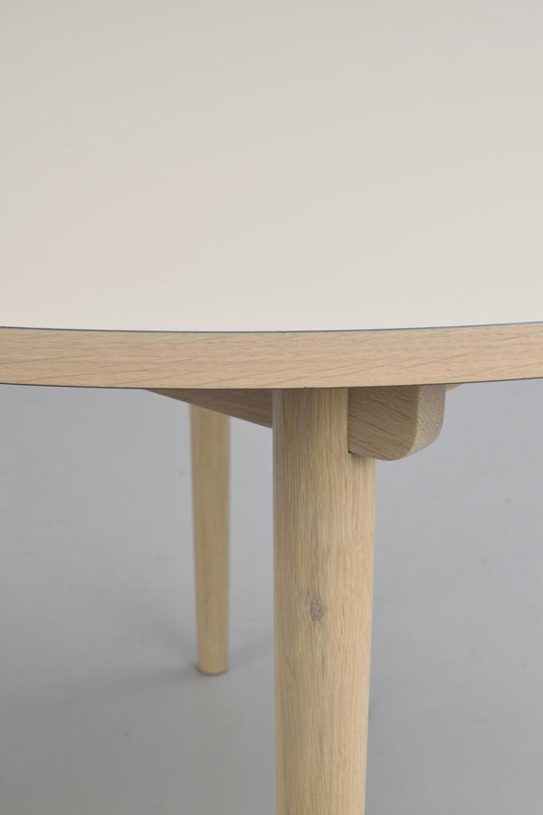 Runt matbord i ljus ek med tre ben och synlig trästruktur, närbild av bordskant och beninfästning