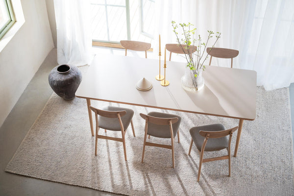 Matbord i ljust trä med sex stolar i skandinavisk design, dekorerat med vas och ljusstakar i minimalistisk matsal