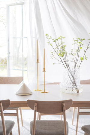 Ljus matsal med träbord, stolar, glaskupa med gröna kvistar och gyllene ljusstakar i skandinavisk stil