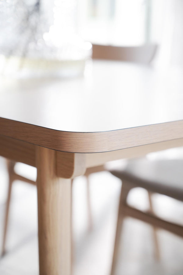 Närbild av träbord med rundade hörn och vita stolar i skandinavisk design