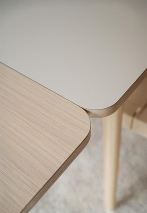 Närbild på två bord med rundade hörn, ett i ljust trä och ett med vit laminatskiva, skandinavisk design