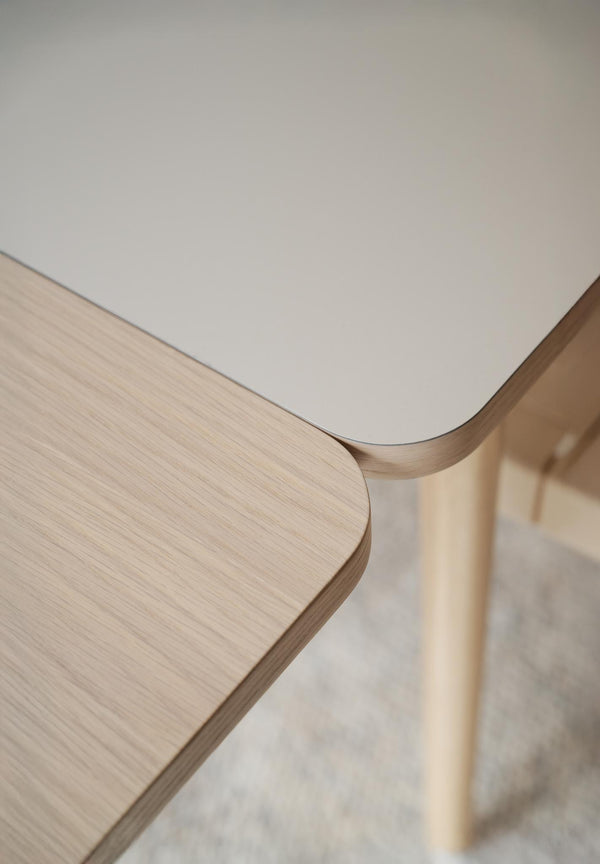 Närbild på två bord med rundade hörn, ett i ljust trä och ett med vit laminatskiva, skandinavisk design