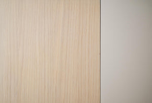 Ljus träfanér med vertikal struktur intill vit vägg, närbild av möbelmaterial