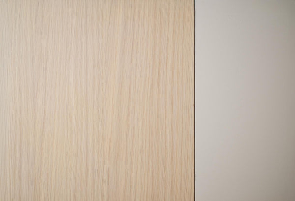Ljus träfanér med vertikal struktur intill vit vägg, närbild av möbelmaterial