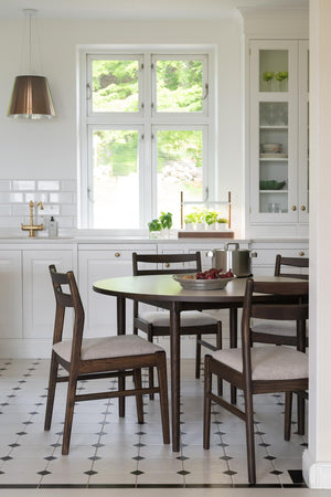 Rund matbord i mörkt trä med fyra stolar och ljusa dynor i modernt kök med vit inredning