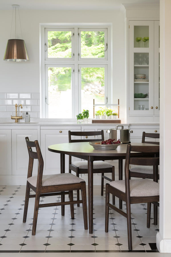 Rund matbord i mörkt trä med fyra stolar och ljusa dynor i modernt kök med vit inredning