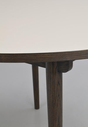 Närbild på möbelskarv i mörkt trä där bordsskiva möter cylindriskt ben med synlig trästruktur