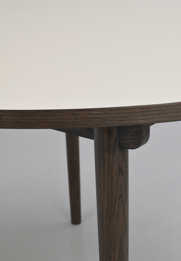 Närbild på möbelskarv i mörkt trä där bordsskiva möter cylindriskt ben med synlig trästruktur