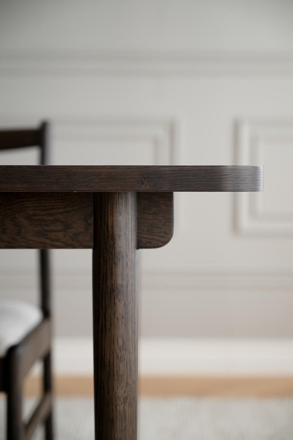 Närbild av mörkbetsad träbord med rundad kant och cylindrisk benställning i modern skandinavisk design