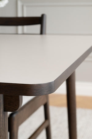 Närbild på matbord med vit laminatskiva och mörkt trästomme, rund hörn detalj