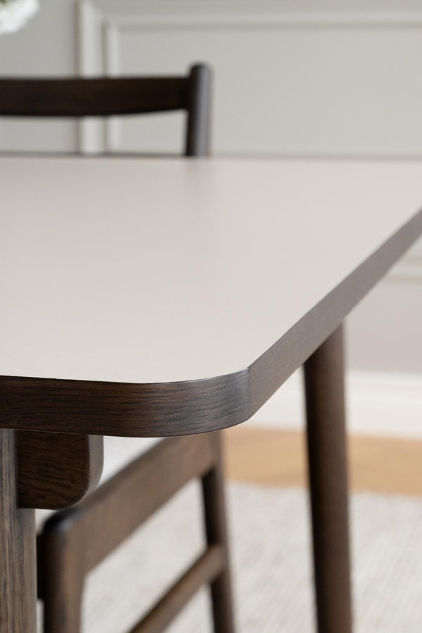 Närbild på matbord med vit laminatskiva och mörkt trästomme, rund hörn detalj