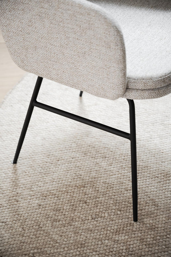 Stol med beige tygsits och svarta metallben på ljus strukturvävd matta