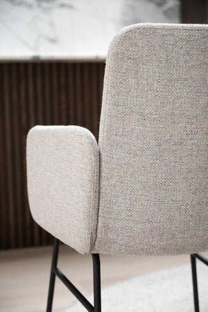 Beige fåtölj med armstöd och svarta metallben i närbild, modern skandinavisk design