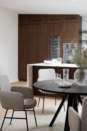 Modern matplats med runt svart bord, grå stolar och brunt kök med integrerade vitvaror i skandinavisk design