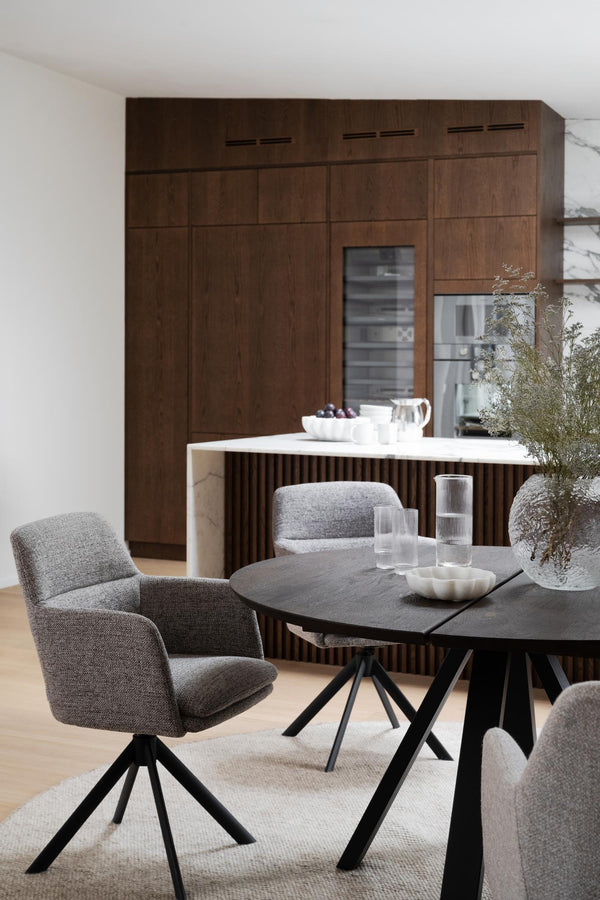 Modern matgrupp med svart bord och grå stolar framför mörkt trä kök med integrerad kyl