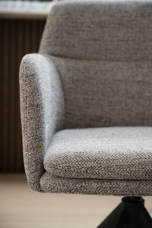 Närbild av grå fåtölj med mjuk klädsel och rundade armstöd i modern skandinavisk design