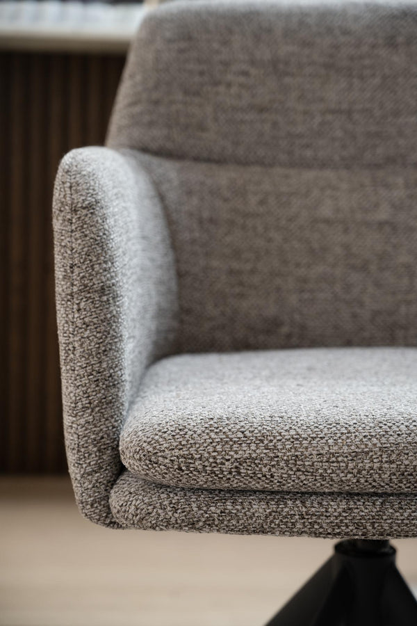 Närbild av grå fåtölj med mjuk klädsel och rundade armstöd i modern skandinavisk design