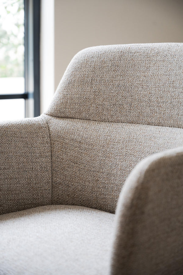 Beige fåtölj i mjukt tyg med rundade former vid fönster med svart ram