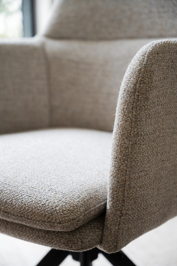 Närbild på beige fåtölj med strukturerad klädsel och svarta ben i modern skandinavisk design