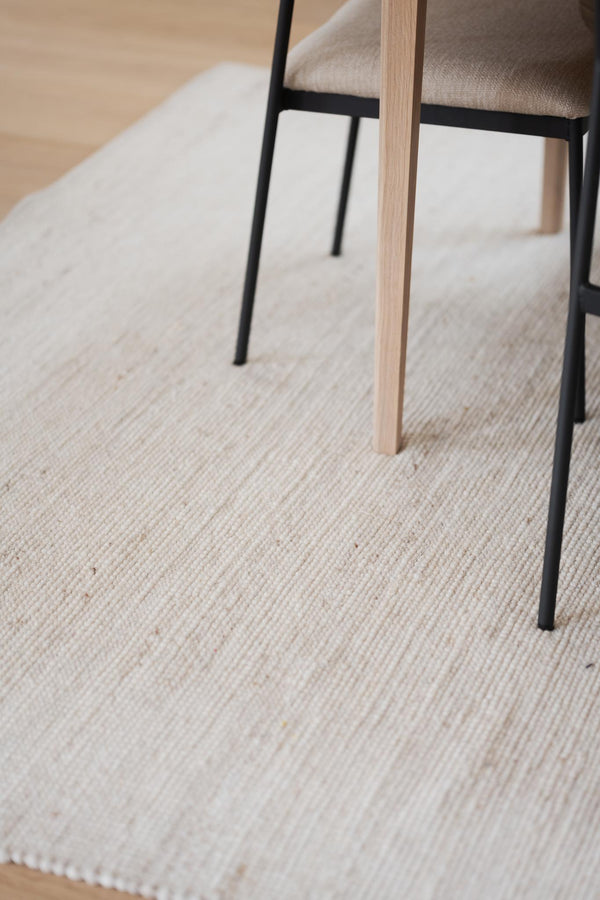 Närbild av stolben i ljust trä och svarta metallben på ljus handvävd matta med struktur