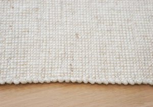 Närbild på vit/beige handvävd ull-matta med texturerad yta mot ljust trägolv