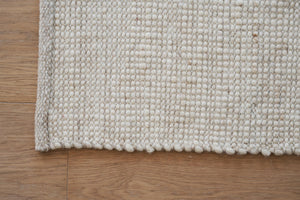 Närbild av ljus vävd matta i naturliga toner på trägolv, visar texturen och strukturen av vävningen