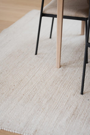 Närbild av stolsben i svart metall och ljust trä på ljus strukturerad matta