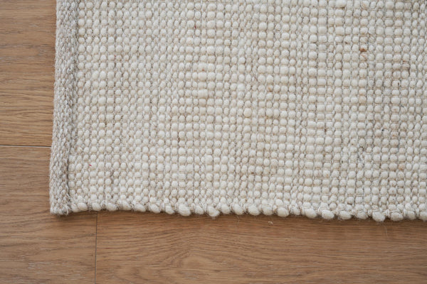 Närbild av ljus handvävd ullmatta med strukturerad yta på trägolv
