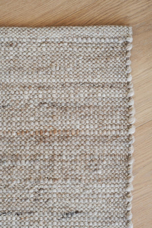 Handvävd matta i beige och bruna toner med strukturerad yta på trägolv