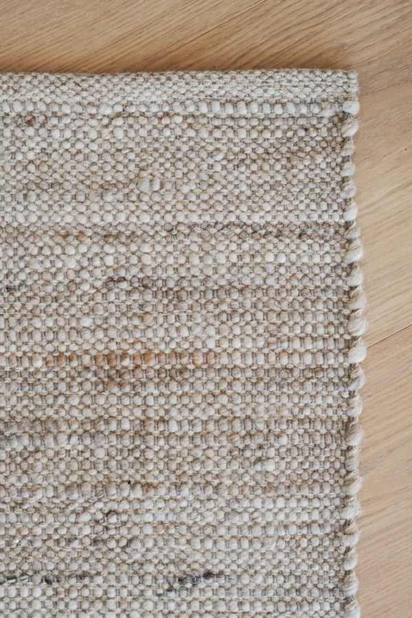 Handvävd matta i beige och bruna nyanser med strukturerad yta på ljust trägolv