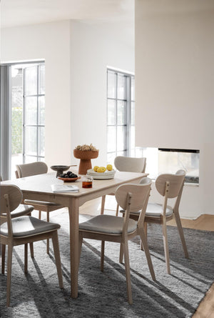 Matbord i ljust trä med sex stolar i grå klädsel, stilren matplats med naturligt ljus från fönster
