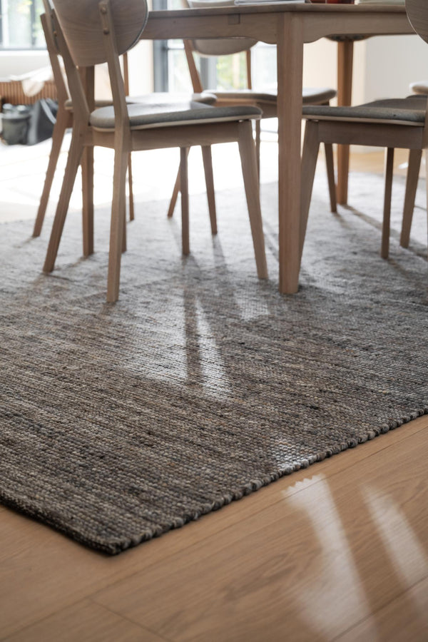 Handvävd grå matta under matbord med träben och stolar med dynor på parkettgolv