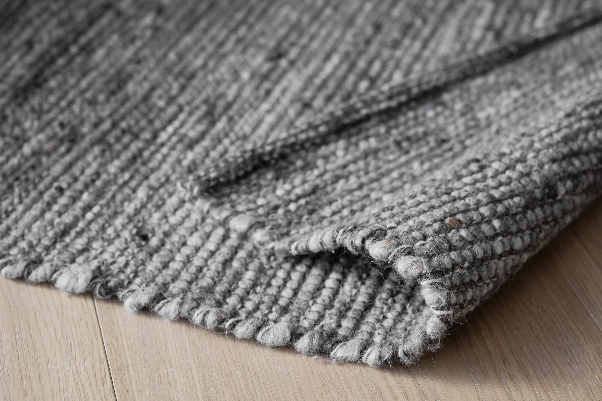Grå stickad filt i ull med tjock struktur och fransar, vikta veck på ljust trägolv