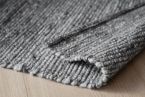 Grov stickad filt i grått med synliga maskor och naturlig textur, vikt på trägolv