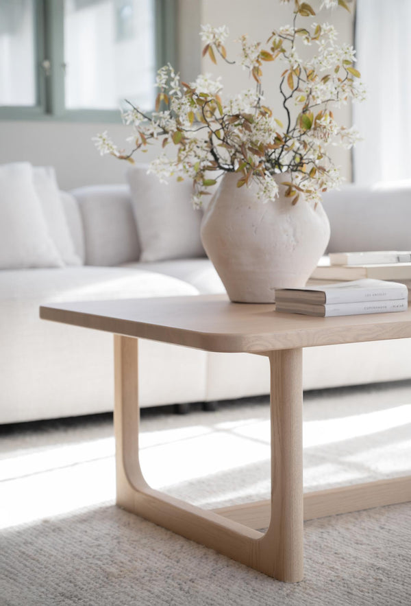 Soffbord i ljust trä med rundade ben och vit keramikvas med vita blommor i modernt vardagsrum