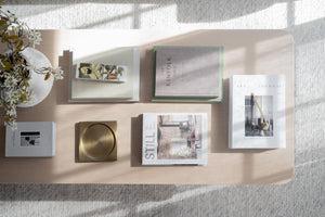 Stilleben med inredningsböcker, dekoration och guldskål på beige soffbord i ljust vardagsrum