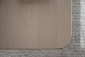 Närbildsdetalj av möbelhörn i ljust trä med rundad kant mot grå matta