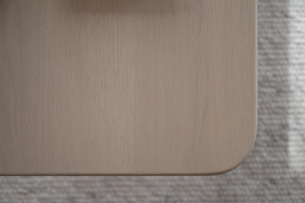 Närbildsdetalj av möbelhörn i ljust trä med rundad kant mot grå matta