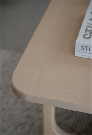 Närbild av soffbord i ljust trä med rundad hörna och synlig trästruktur, trendigt skandinaviskt design