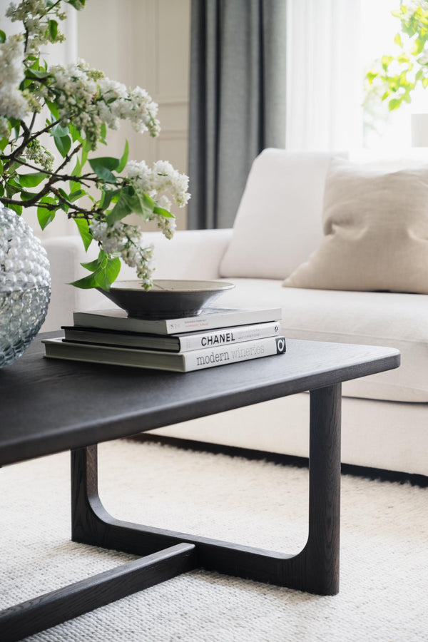 Soffbord i mörkt trä med böcker och vita blommor i modern vardagsrumsinredning